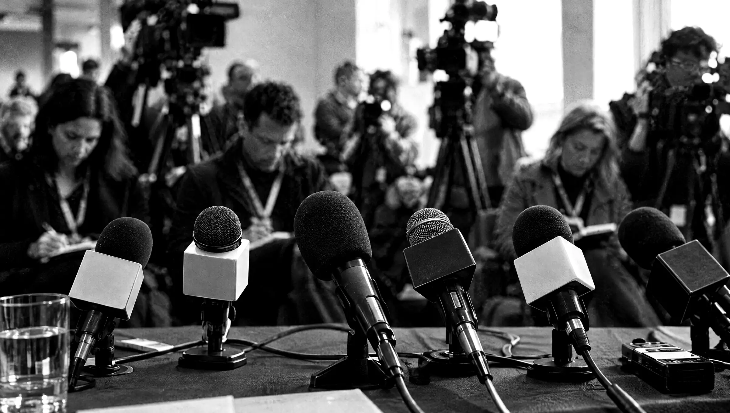 Microphones lined up at a press conference with journalists behind